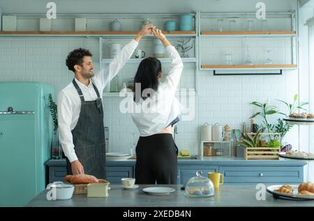 Ein Ehemann trägt eine Schürze, während er mit seiner Frau ein Abendessen kocht. Er tanzte fröhlich, bevor er in die Küche ging, um zu kochen. Stockfoto