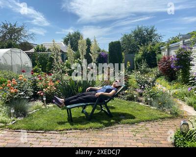 Frau, die auf einem Gartenlehnstuhl im Garten des Hauses liegt Stockfoto