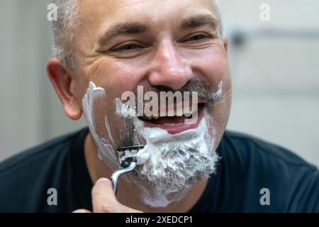 Ein hübscher Mann mittleren Alters, der sich im Badezimmer den Bart rasiert Stockfoto