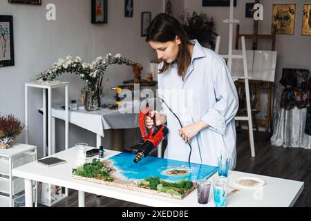 Künstler, der eine Heißluftpistole auf Epoxidharz-Küstenkunstwerken verwendet Stockfoto