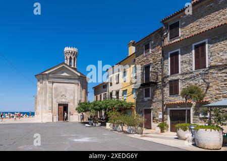 Die Küstenstadt Piran in Slowenien. Platz mit der Kirche unserer Lieben Frau der Gesundheit und traditionellen Häusern am Ufer von Presernovo Nabrezje, Adriaküste, Stockfoto