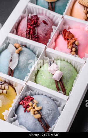 Köstliche süße bunte Mochi-Desserts oder Eis mit Reisteig und Belägen in einer Pappschachtel auf einem dunklen Betonhintergrund Stockfoto