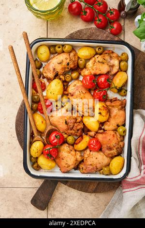 Hähnchenschenkel gebacken mit neuen Kartoffeln, Kirschtomaten und Oliven in Weißwein Burgunderstil in rustikaler Backform und Holzhintergrund. Abdeckung oder AR Stockfoto