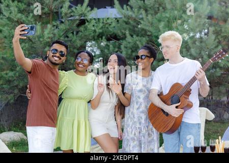 Eine Gruppe multirassischer Freunde, die Spaß haben und Wein trinken, während sie Selfies beim Sommer-Picknick machen. Stockfoto