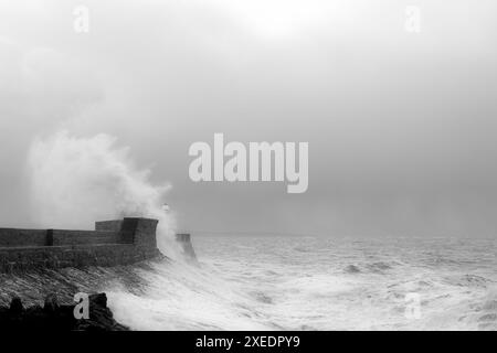 Schwarzweiß-Bild einer Welle, die über Porthcawls Wellenbrecher und Leuchtturm stürzt. Es ist Versteck-Flut an einem frühen Wintermorgen. Stockfoto