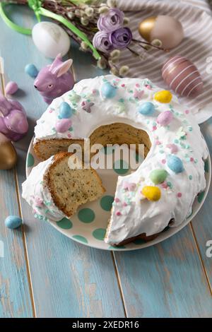 Glasierter osterzitronenkuchen, dekoriert mit Süßwaren und Mini-Schokoladeneiern auf einem Holztisch. Stockfoto