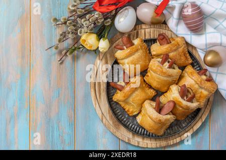Brötchen in Form eines Osterkaninchens und farbige Eier auf einem Holztisch. Stockfoto