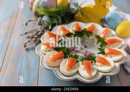 Gefüllte Eier mit Käse und gesalzenem Lachs in Form einer Karotte auf einem Holztisch. Stockfoto