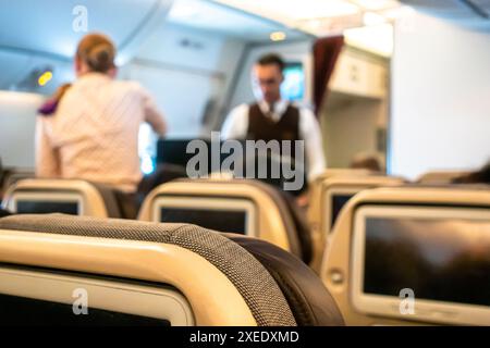 Zwei Flugbegleiter, männlicher Steward und weiblicher Stewardess servieren den Passagieren Getränke, die auf einem Stuhl in einer Flugzeugkabine der Boeing 787-10 Etihad sitzen Stockfoto