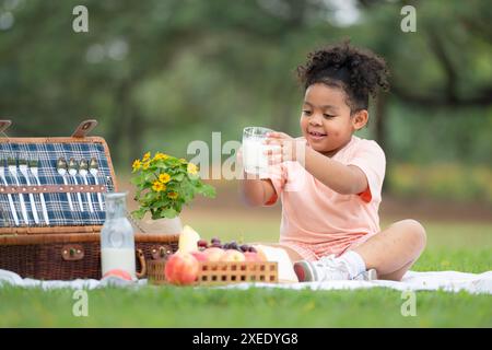 Glückliche Familie, die ein Picknick im Park genießt, während Kinder Milch trinken, umgeben von der Natur Stockfoto