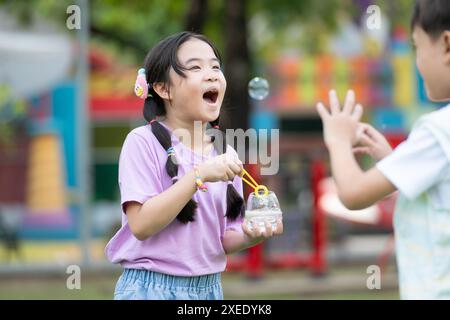 Kinder sitzen im Park mit bläsender Luftblase, umgeben von Grün und Natur Stockfoto