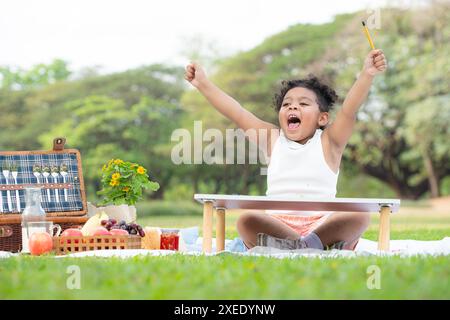 Glückliche Familie, die ein Picknick im Park genießt, Mädchen haben Spaß beim Zeichnen auf Papier, das auf den Tisch gelegt wird. Stockfoto