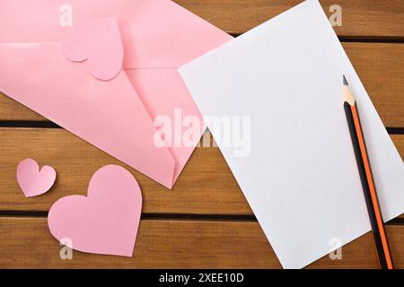 Detail des leeren Liebesbriefes auf Holztisch mit rosa Umschlag und Herzausschnitten. Draufsicht. Stockfoto