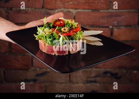 Thunfisch-Tatar serviert mit Toast und Salat auf schwarzem Steinteller Stockfoto