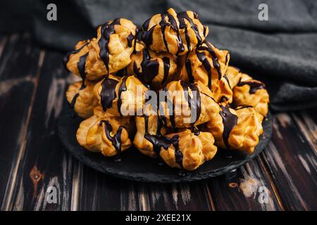 Profiterolen mit Schokoladencreme auf schwarzer Platte Stockfoto