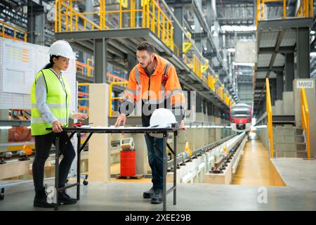 Männliche und weibliche Ingenieure arbeiten in einer elektrischen Reparaturstation zusammen. Prüfen Sie die Details des Reparaturplans für elektrische Züge. Stockfoto