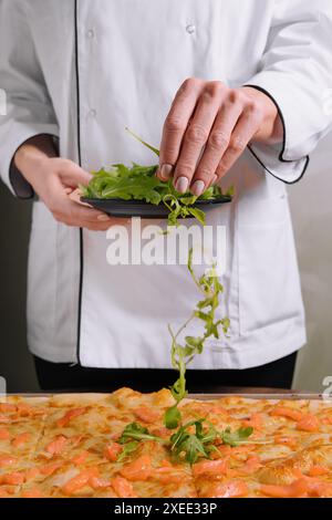 Der Koch dekoriert Lachspizza mit Rucola Stockfoto