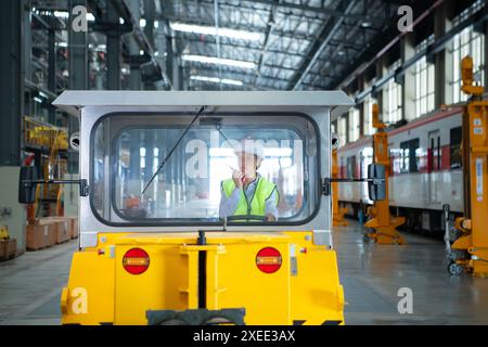 Weibliche Ingenieurin, die in einer Elektrobahn-Werkstatt arbeitet, testen Sie das Fahren eines kleinen Schleifens der Eisenbahnschienen-Maschine, bevor Sie pu werden Stockfoto