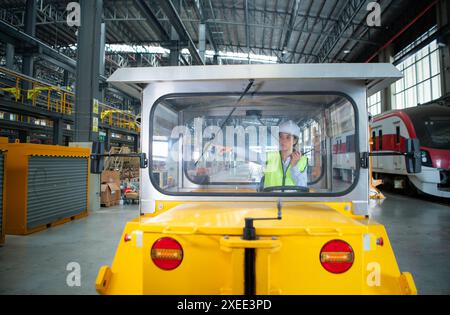 Weibliche Ingenieurin, die in einer Elektrobahn-Werkstatt arbeitet, testen Sie das Fahren eines kleinen Schleifens der Eisenbahnschienen-Maschine, bevor Sie pu werden Stockfoto