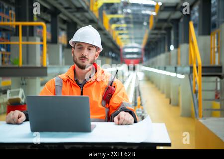 Porträt des jungen männlichen Technikers, der auf dem Tisch in der Skytrain-Reparaturstation sitzt, überprüfen Sie die Details der elektrischen Bahn repai Stockfoto