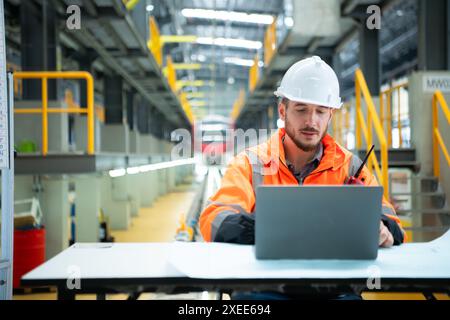Porträt des jungen männlichen Technikers, der auf dem Tisch in der Skytrain-Reparaturstation sitzt, überprüfen Sie die Details der elektrischen Bahn repai Stockfoto