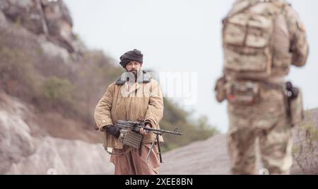 Ein Taliban-Soldat steht mit einem Maschinengewehr auf dem Schlachtfeld in den Bergen der Wüste und ergibt sich den alliierten Soldaten Stockfoto