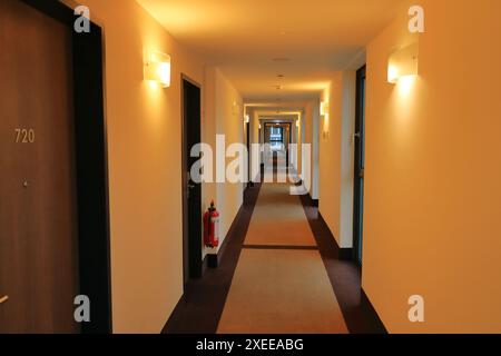 Ein leerer langer Hotelkorridor mit Teppichboden und Lampen beleuchtet die vertikale Innenansicht der Gebäudearchitektur Stockfoto