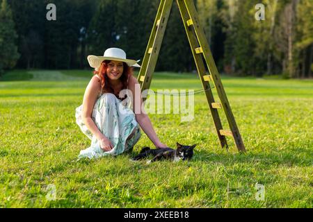 Frau auf einer Wiese mit einer Leiter, die eine Katze streichelt Stockfoto