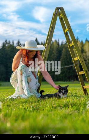 Frau auf einer Wiese mit einer Leiter, die eine Katze streichelt Stockfoto