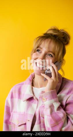 Lächelnde Frau Mit Nase Piercing, Die Auf Handy Vor Gelbem Studio-Hintergrund Spricht Stockfoto