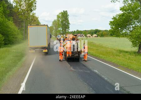 Tarnow, Polen - 19. Mai 2023: Straßenarbeiter in reflektierenden Westen bedienen auf einer Landstraße Straßenpflastermaschinen mit vorbeifahrenden Fahrzeugen. Stockfoto