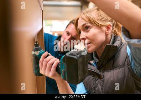 Zimmermann Mit Weiblicher Auszubildender In Der Werkstatt Mit Bohrer Zum Befestigen Eines Holzstücks Am Fensterrahmen Stockfoto