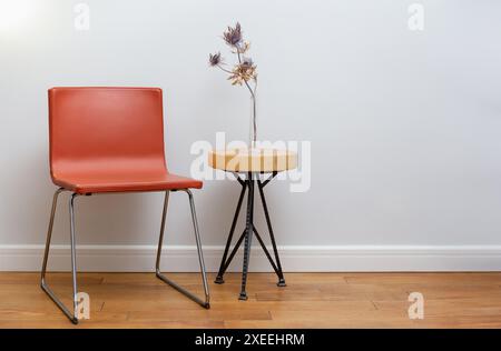 Roter Stuhl und hölzerner Couchtisch mit Blumenvase in minimalistischem Innenraum, helle Wand Stockfoto