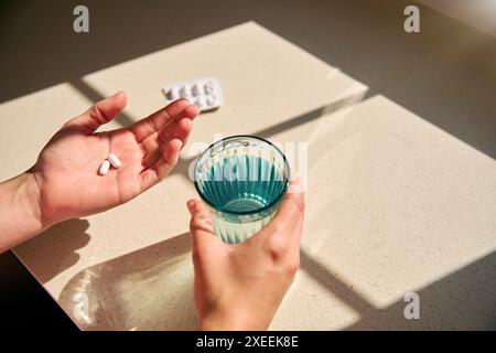 Nahaufnahme, Die Auf Die Frau Herabblickt, Die Zu Hause Medikamente Einnimmt, Mit Einem Glas Wasser Im Sonnenlicht Stockfoto