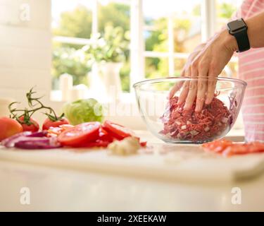 Nahaufnahme Einer Frau Zu Hause, Die Eine Mahlzeit In Der Küche Zubereitete Und Frische Zutaten In Der Schüssel Mit Fleisch Ergänzte Stockfoto