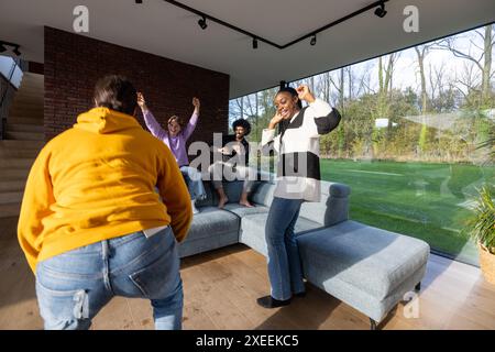 Fröhliche Freunde tanzen zusammen in einem hellen, modernen Wohnzimmer Stockfoto