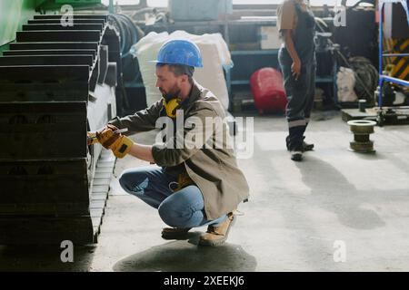 Bärtiger männlicher Mechaniker, der Teil des modernen Planierraupenfahrwerks bei der Arbeit in der industriellen Werkstatt, im Kopierraum Stockfoto