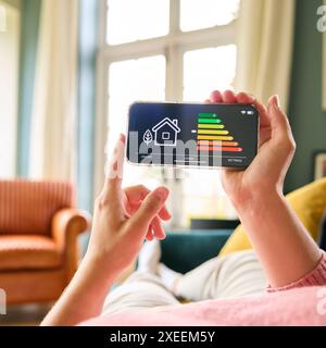 Nahaufnahme Einer Frau, Die Auf Dem Bildschirm Des Energieeffizienzmessers Auf Dem Mobiltelefon Auf Dem Sofa Zu Hause Liegt Stockfoto