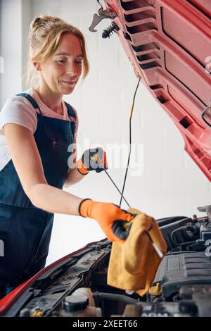 Weibliche Automechanikerin, Die Unter Der Motorhaube Des Fahrzeugs Nachsieht Und Den Ölstand Mit Dem Messstab Überprüft Stockfoto