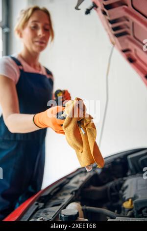 Weibliche Automechanikerin, Die Unter Der Motorhaube Des Fahrzeugs Nachsieht Und Den Ölstand Mit Dem Messstab Überprüft Stockfoto