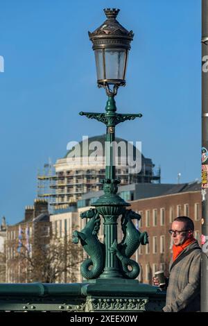 Mann, der an gusseisernen Seepferden aus dem 19. Jahrhundert auf der Grattan-Brücke mit vier Höfen im Hintergrund vorbeiläuft, Dublin, Irland Stockfoto