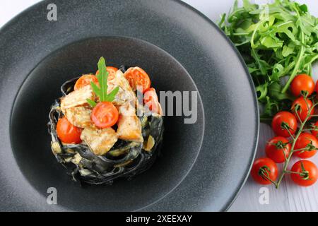 Schwarze Spaghetti. Schwarze Nudeln mit Meeresfrüchten auf weißem Teller auf schwarzem Hintergrund mit Kopierraum. Stockfoto