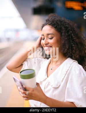 Geschäftsfrau Pendelt Auf Bahnsteig Mit Handy Und Wiederverwendbarer Kaffeetasse Stockfoto