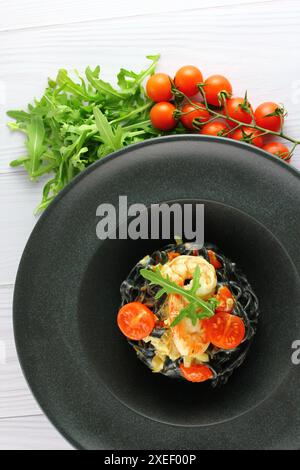 Schwarze Spaghetti. Schwarze Nudeln mit Meeresfrüchten auf weißem Teller auf schwarzem Hintergrund mit Kopierraum. Stockfoto