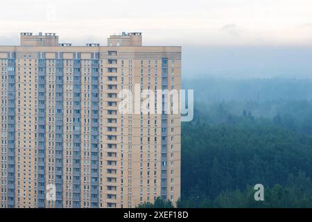 Hochhaus-Wohngebäude in einem neuen Gebiet, ein neues Gebäude am Stadtrand in der Nähe des Waldes an einem nebeligen Morgen, Blick von unten Stockfoto