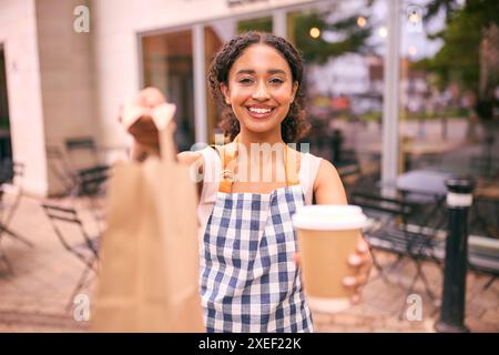 Porträt Einer Frau, Die Eine Schürze Vor Dem Café Oder Café Trägt, Die Heiße Getränke Und Speisen Zum Mitnehmen Hält Stockfoto