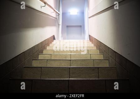 Stufen führen nach oben und eine Ampel am Ende des Korridors mit einem leuchtenden Ausstiegsschild. Ein Flur mit Treppen, beleuchtet durch Lampen, Geländer, Tür am en Stockfoto