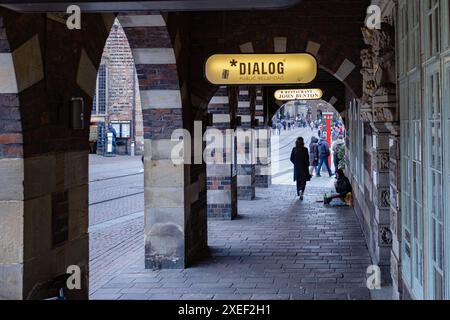 Bremen, Deutschland - 11.03.2023: Straße einer Großstadt, Bogen mit Säulen, Leute gehen die Straße hinunter, reiner Mann sitzt auf dem Boden mit einer Flasche Wein, Stockfoto