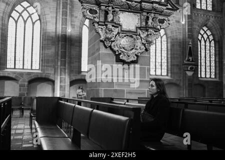 Junge Frau betet in der katholischen Kirche. Die schöne Frau kam zu Gott und fragte, was zu tun sei. Der alte Dom in Deutschland. Schwarzweißbild. Stockfoto