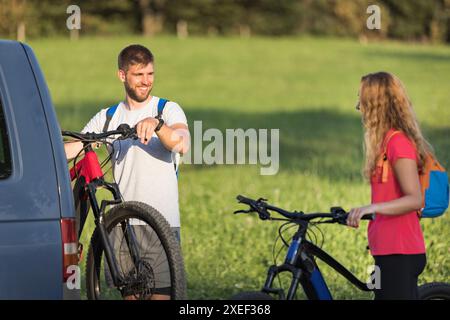 Ein junger Mann und eine Frau bereiten sich auf das Geländeradfahren vor und nehmen Elektro-Mountainbikes vom Fahrradträger im Wohnmobil ab. Stockfoto